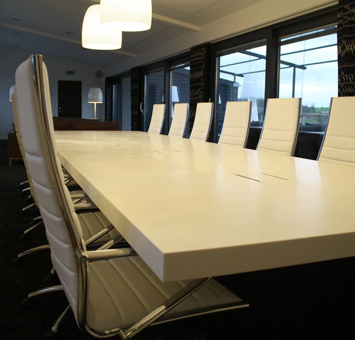 Mødebord udført i Corian, med integreret kabelbrønde for tilkobling af pc, bordet hviler på en sort sokkelkasse