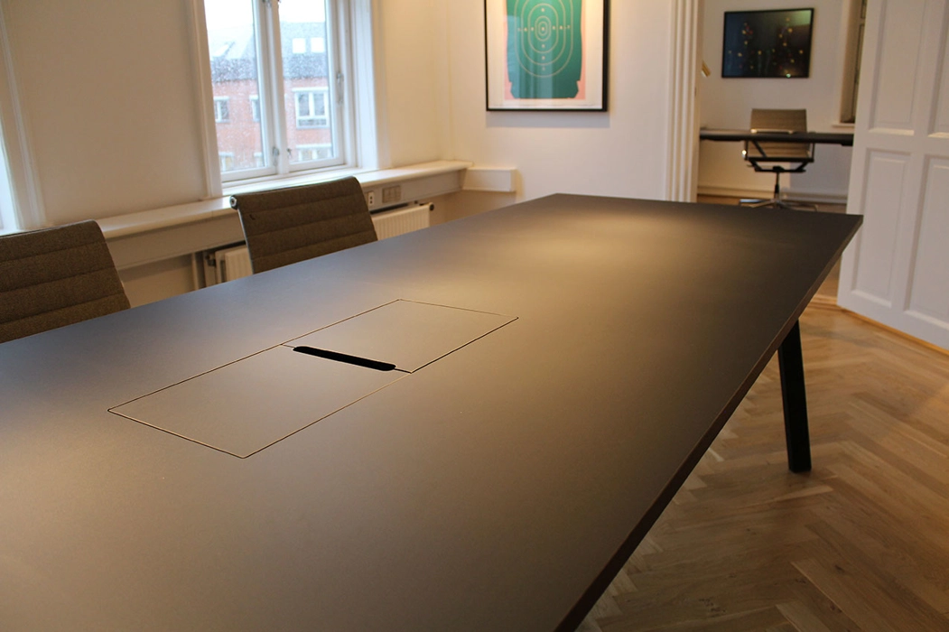 Mødebord udført i sort linoleum, men integreret kabelbrønd for tilslutning af pc, bordet er med sorte stålben.